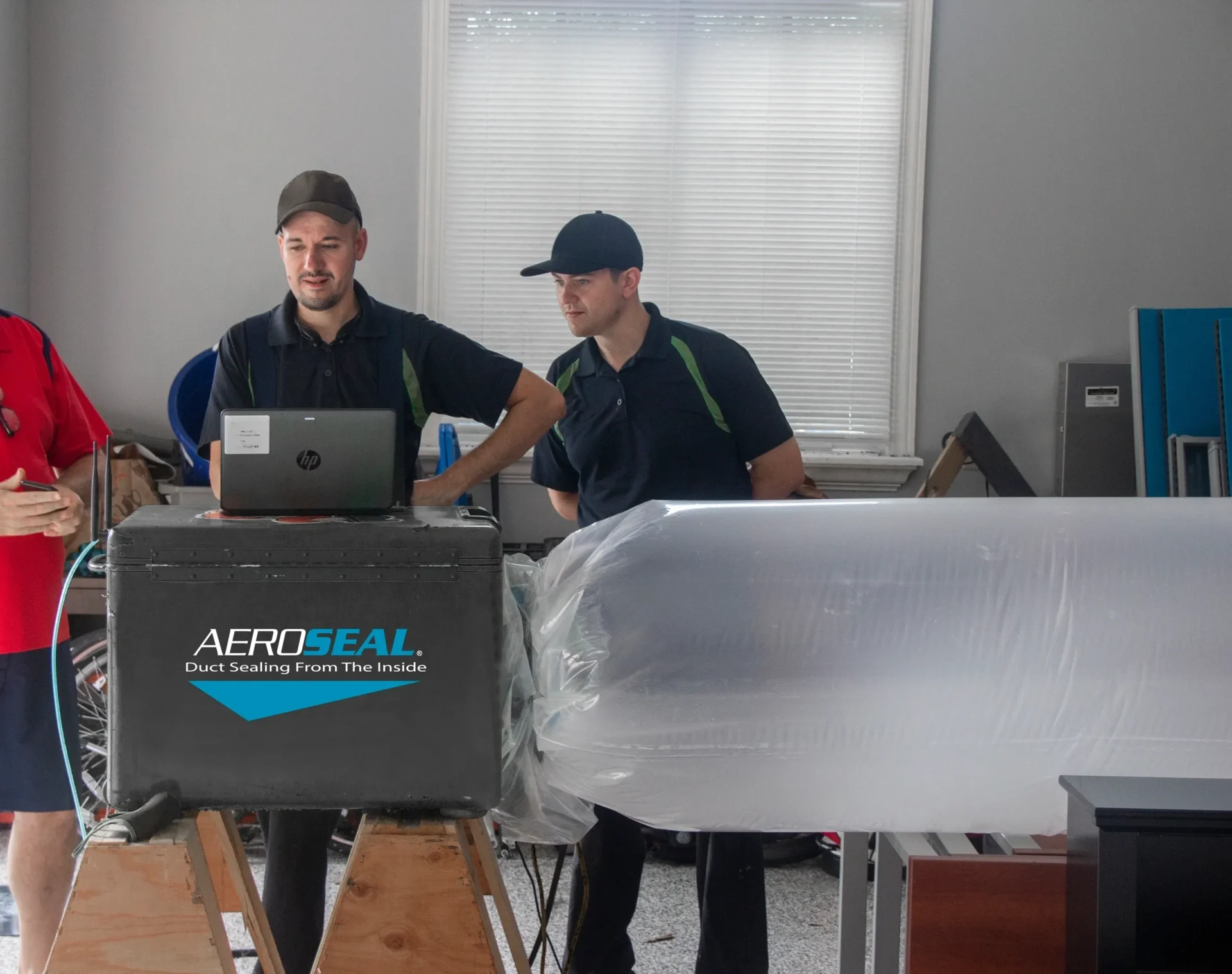 Two men in black shirts and hats working on a laptop.