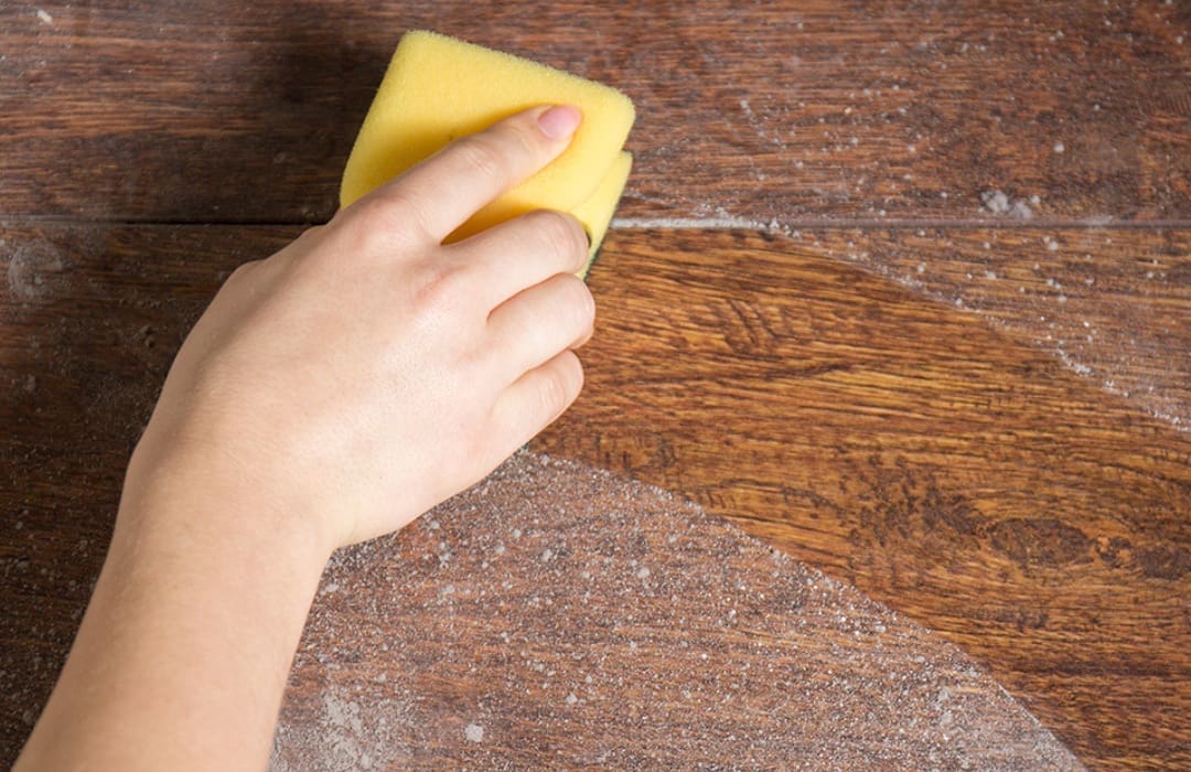 A person cleaning the wood floor with a sponge.