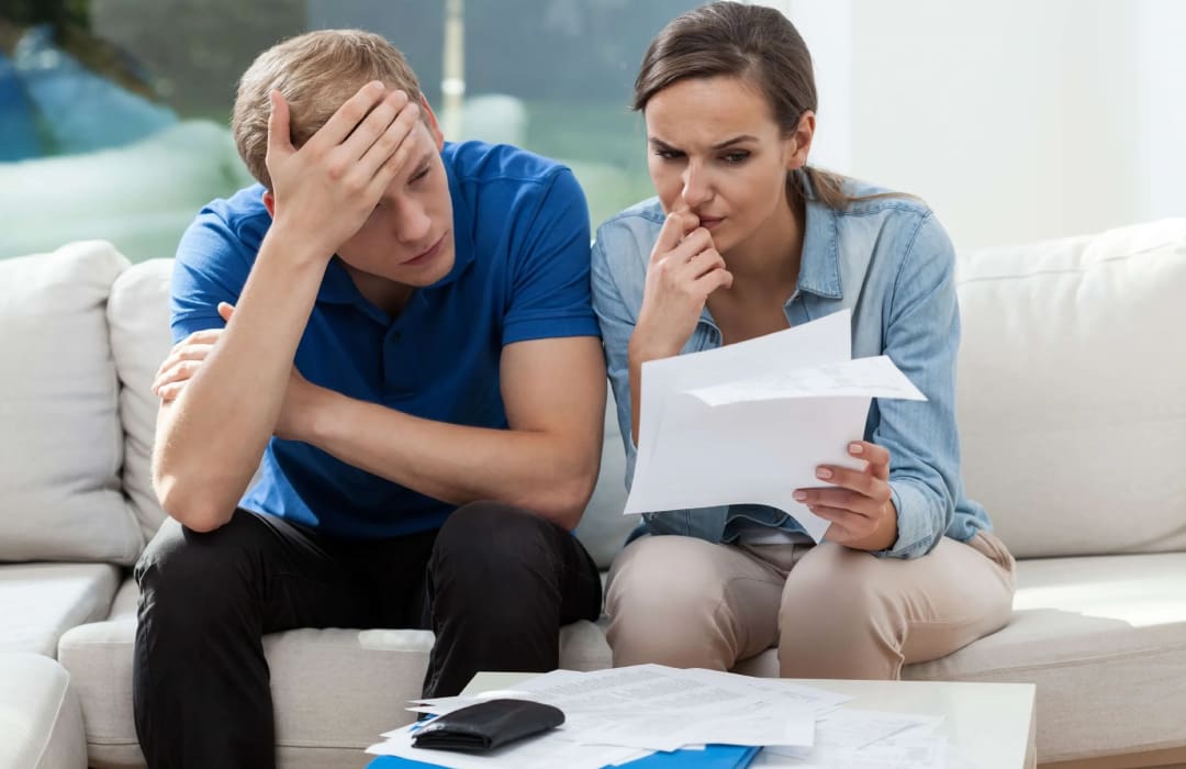 A man and woman sitting on the couch looking at papers.